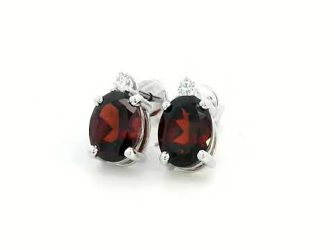 18K white gold garnet and diamond stud earrings featuring oval-cut 3.09-carat garnets with 0.07-carat diamond accents, set in a classic four-prong setting with push-back closures.