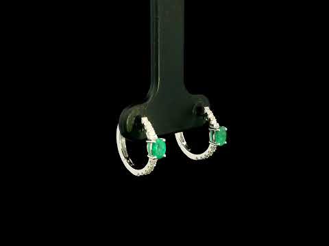 18K white gold emerald and diamond huggie hoop earrings featuring oval green emeralds and diamond-set hoops.