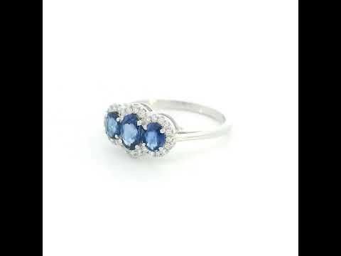 Three stone blue sapphire ring in 18K white gold featuring oval sapphires surrounded by individual diamond halos.