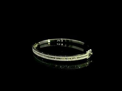 18K white gold diamond bangle with a central row of baguette diamonds framed by round brilliant diamonds and secure hinged clasp