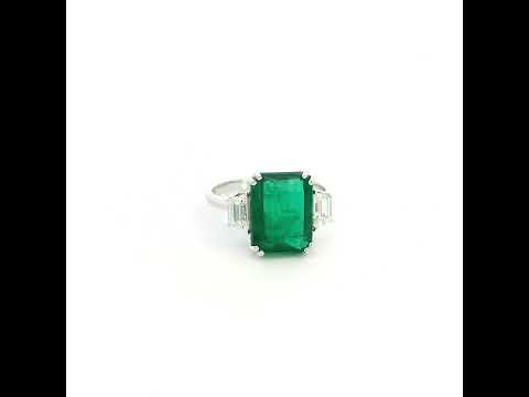 Emerald cut natural emerald and trapezoid diamond three stone ring in 18K white gold featuring a 4.77 carat emerald and 0.75 carat diamonds