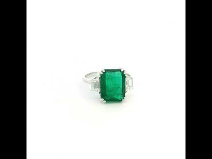 Emerald cut natural emerald and trapezoid diamond three stone ring in 18K white gold featuring a 4.77 carat emerald and 0.75 carat diamonds