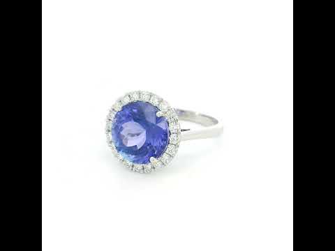 Round tanzanite and diamond halo ring in 18K white gold featuring a 5.97 carat violet-blue tanzanite surrounded by round diamonds on a polished band.
