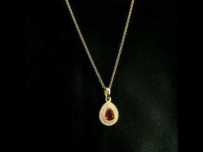 Ruby and diamond halo pendant in 18K yellow gold with a pear-shaped red ruby surrounded by two rows of round diamonds