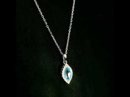Blue topaz and diamond halo pendant in 18K white gold featuring a 0.70 carat oval blue topaz surrounded by 0.15 carat round diamonds in an elongated marquise-shaped setting, shown with a chain for display.