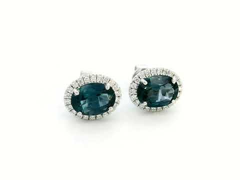 8K gold stud earrings featuring 2.90 carats of oval London Blue Topaz, encircled by a 0.25-carat diamond halo. Classic elegance with secure push-back closure.